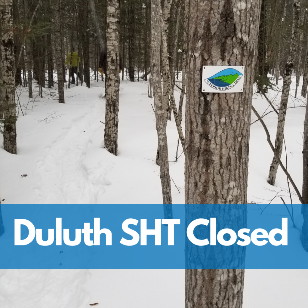 A tree with an SHT marker in front of snow-covered ground and a banner that reads "Duluth SHT Closed"